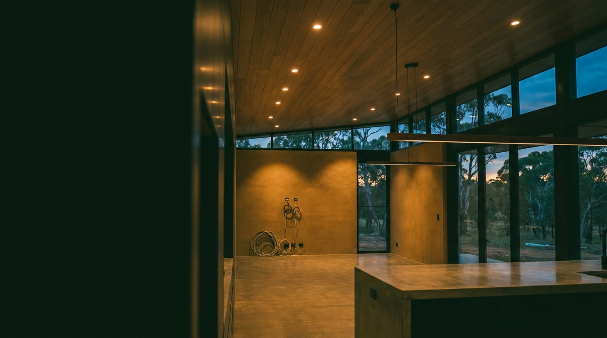 A new build interior at dusk with downlights on across a raked timber ceiling