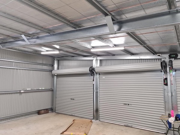 A newly finished shed with roller doors, lit by batten lights across the roof frame