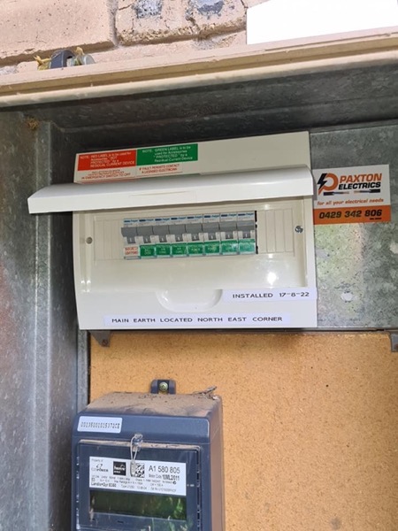 A switchboard fitted with a Paxton Electrics sticker beside a wall-mounted meter