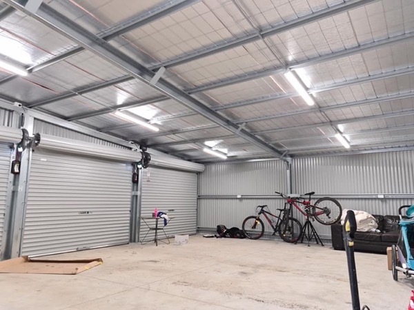 The inside of a large shed with rows of batten lights fitted along the roof frame