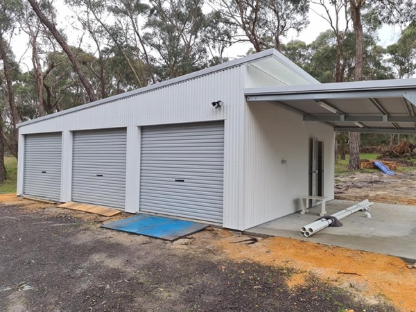 A newly built shed with three roller doors, surrounded by gum trees