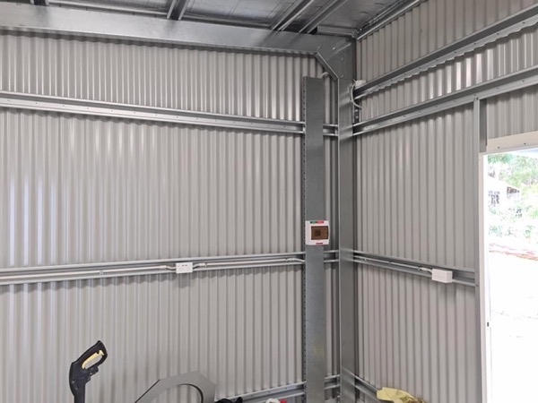 The inside of a shed with power points and batten lighting fitted along the wall frame