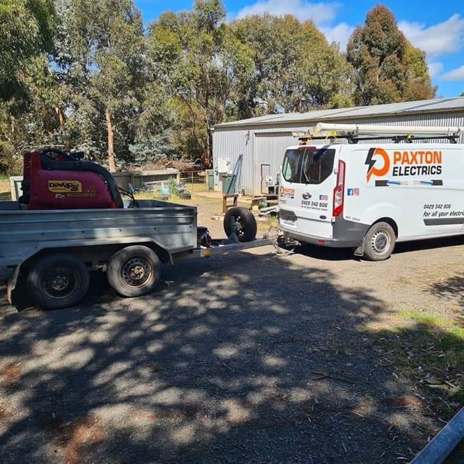 Two Paxton Electrics vans and a work trailer parked on a gravel driveway among gum trees