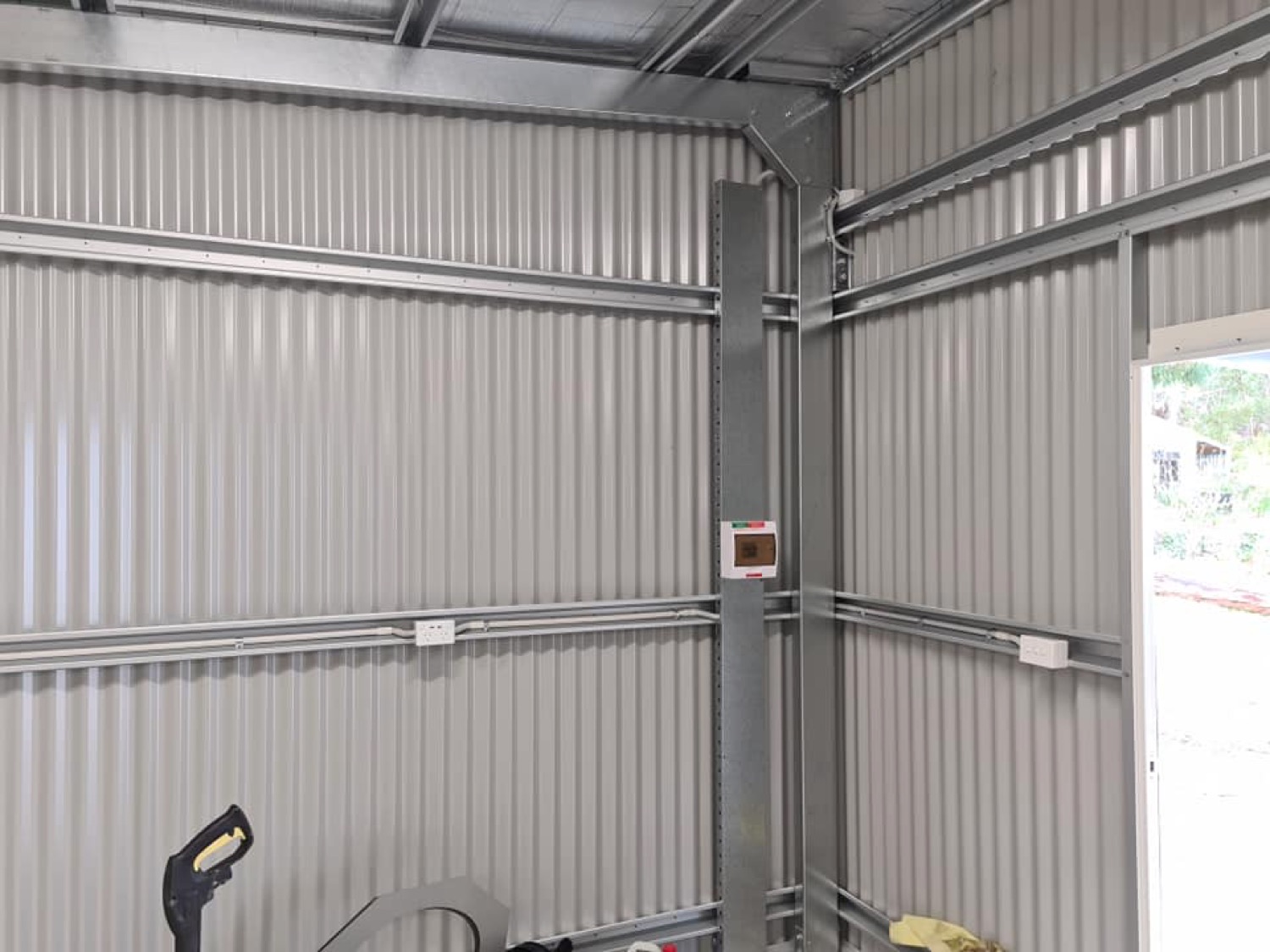 The inside of a shed with power points and batten lighting fitted along the wall frame